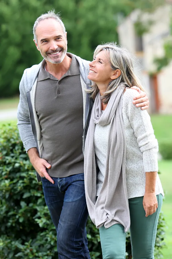 Bioidentical-Hormone-Therapy-Treatment A mature couple in gray toned clothes and jeans walk happily outside, happy with their successful bioidentical hormone treatments from Marina Fay, PA-C in Aventura-North Miami.