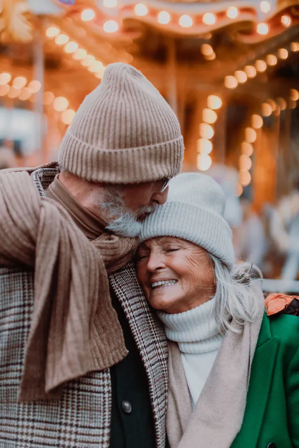 Cognitive-Decline-Treatment A mature couple in winter clothes embrace by a carousel. Get cognitive decline treatment from Marina Fay, PA-C in Aventura-North Miami.