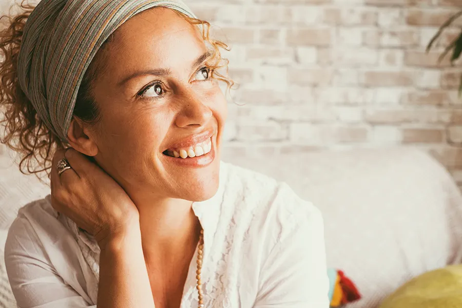 Exosome-Facial-Clinic A beautiful middle-aged mixed-race woman smiling in her living room. Get exosome facial treatment from Marina Fay, PA-C in Aventura-North Miami.