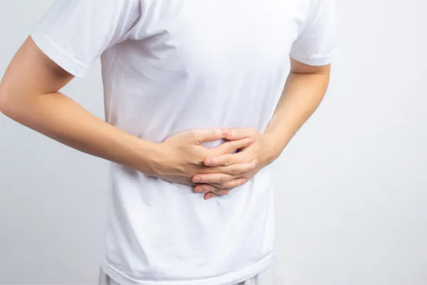 Irritable-Bowel-Syndrome-Clinic A person holding their stomach in visible discomfort against a plain background. Marina Fay, PA-C treats irritable bowel syndrome with functional medicine in Aventura-North Miami.