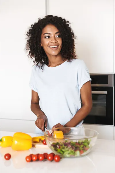 Irritable-Bowel-Syndrome-Treatment Image featuring a smiling woman chopping vegetables for a salad in a bright, white kitchen. Marina Fay, PA-C offers Irritable Bowel Syndrome Treatment and Digestive Support in Aventura-North Miami.