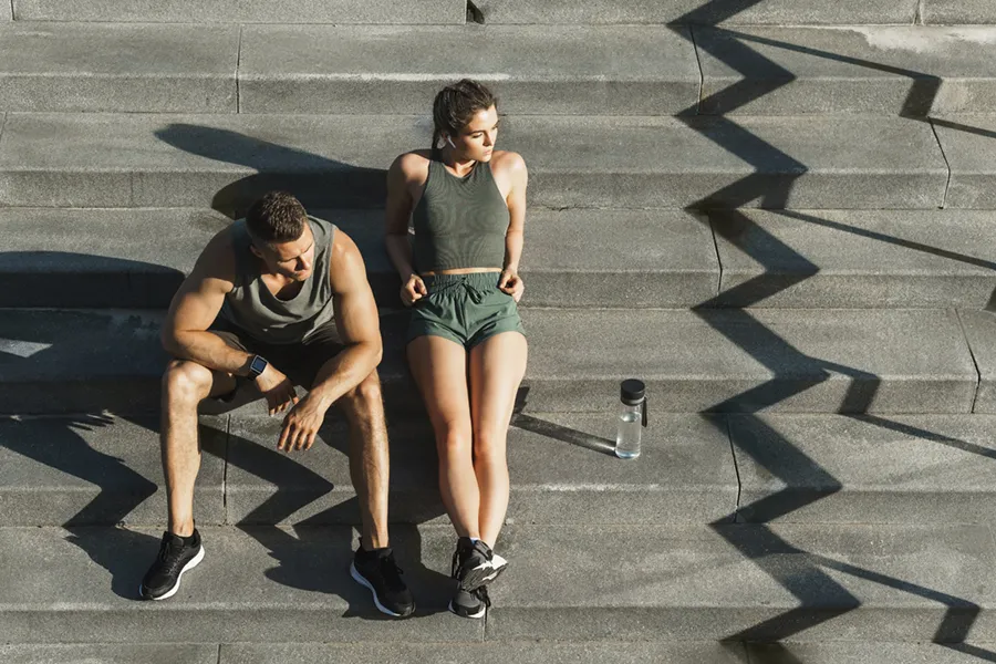 Medical-Weight-Loss-Doctor A couple in gray and green track clothes resting after a workout on stone steps, happy with their weight loss plans from Marina Fay, PA-C in Aventura-North Miami.