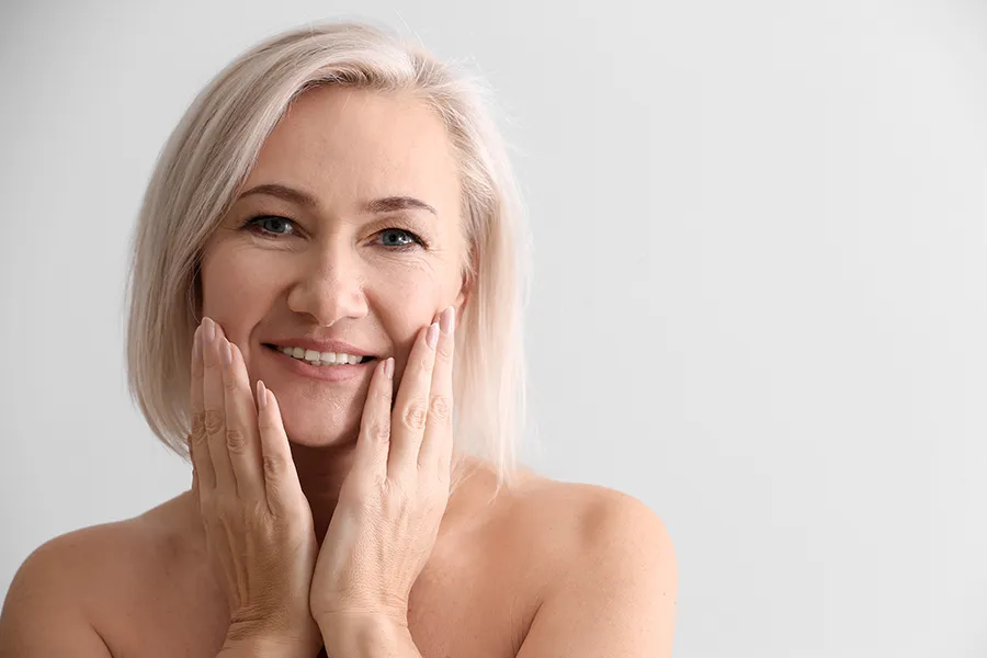 PRP-Microneedling-Clinic A mature woman touches her faces to feel the successful results of PRP microneedling and skin rejuvenation treatments from Marina Fay, PA-C in Aventura-North Miami.
