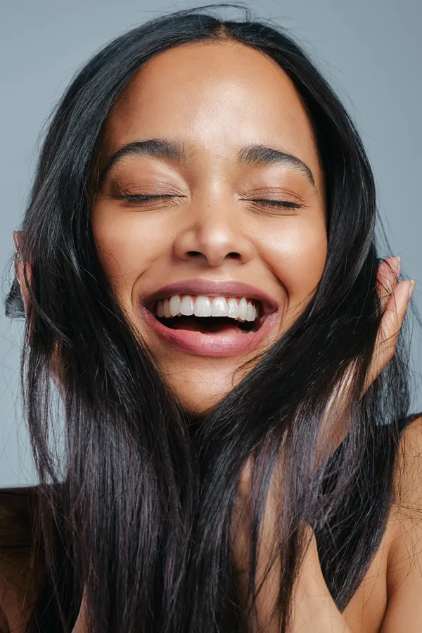 PRP-for-Hair-Loss-Treatment A beautiful latin woman smiles and runs her fingers through her long, beautiful hair, happy with her PRP for hair loss and restoration treatment from Marina Fay, PA-C in Aventura-North Miami.