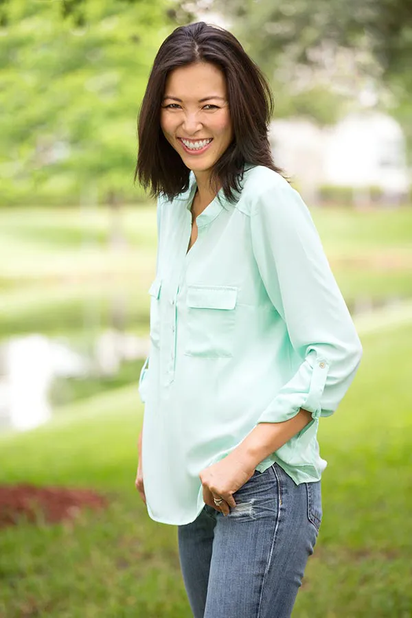 Perimenopause-Treatment A middle-aged brunette woman in a light green button-up shirt stands outside smiling, happy with her perimenopause treatment from Marina Fay, PA-C in Aventura-North Miami.