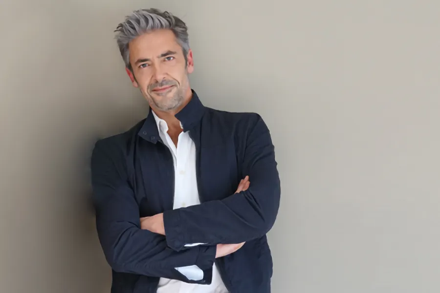Testosterone-Low-T-Solutionsn-Clinic A middle-aged man in a white shirt and dark blue jacket leans against a gray wall smiling. Get testosterone for Low T from Marina Fay, PA-C in Aventura-North Miami.
