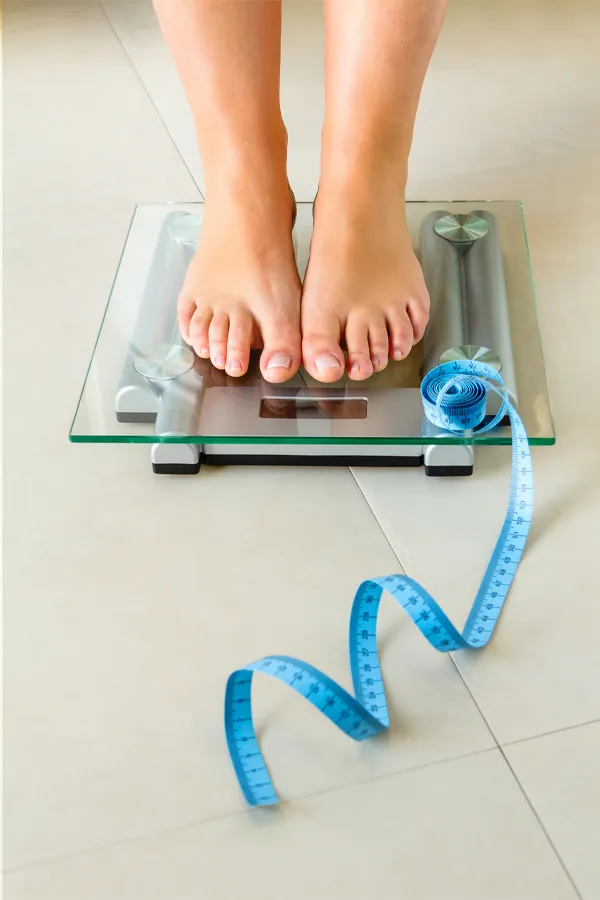 Weight-Loss-Resistance-Treatment Close-up of a woman's feet standing on a scale, with measuring tape by her toes, getting treatment for weight loss resistance from Marina Fay, PA-C in Aventura-North Miami.